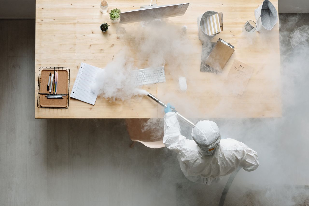 An individual is disinfecting a workspace by fumigation while wearing full protective equipment for safety.